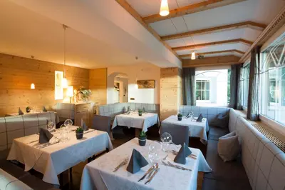 a restaurant with white tables and chairs and windows at Hotel Comploj Adults only in Selva di Val Gardena