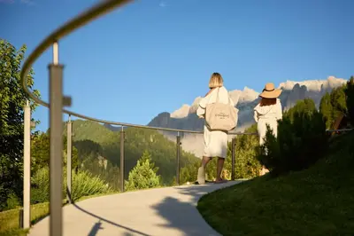 three women in white walking down a walkway with mountains in the background at Hotel Comploj Adults only in Selva di Val Gardena