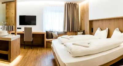 a hotel room with two beds and a desk at Hotel Des Alpes in Selva di Val Gardena