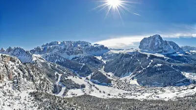 a snowy mountain range with the sun in the sky at Hotel Des Alpes in Selva di Val Gardena