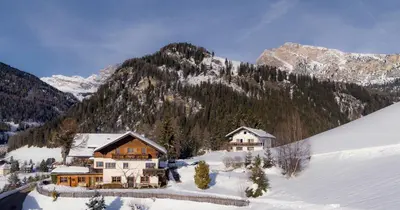 a house in the snow in front of a mountain at Villa al Bosco in Selva di Val Gardena