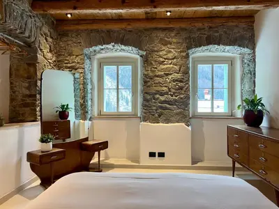 a bedroom with a stone wall with a bed and two windows at Appartamenti La Rocia in Rocca Pietore