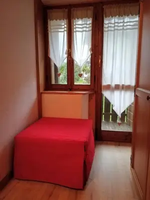 a red bed in a room with two windows at CASA VACANZE MIRAMONTI - appartamento con balcone con vista sulle Dolomiti in Borca di Cadore