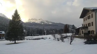 a snow covered yard with a building and a mountain at CASA VACANZE MIRAMONTI - appartamento con balcone con vista sulle Dolomiti in Borca di Cadore