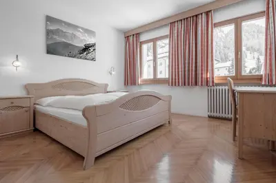 a bedroom with a bed and a table and windows at ARTEFUGIUM panoramico in Selva di Val Gardena