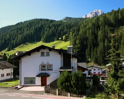 a white house with a green hill in the background at ARTEFUGIUM panoramico in Selva di Val Gardena