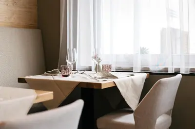 a table with white chairs and a table with a window at Weingut & Genusshotel Spitalerhof Superior in Chiusa
