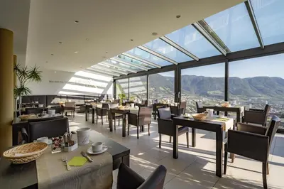 a restaurant with tables and chairs and windows at Hotel Lechner in Tirolo