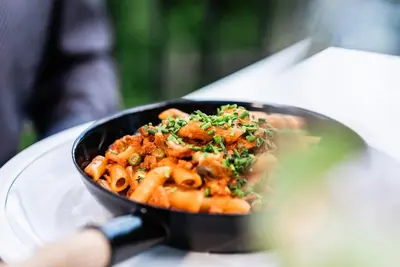 a person holding a pan of pasta on a plate at Hotel Tannhof in Caldaro