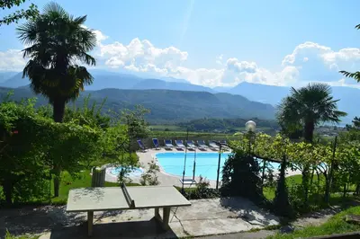 a bench next to a swimming pool with mountains in the background at Hotel Tannhof in Caldaro