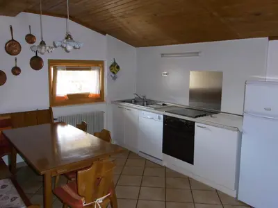 a kitchen with white appliances and a wooden table at Casa Elisa in Pozza di Fassa