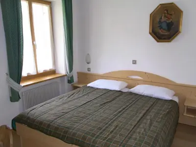 a bedroom with a bed with a green blanket and two windows at Casa Elisa in Pozza di Fassa