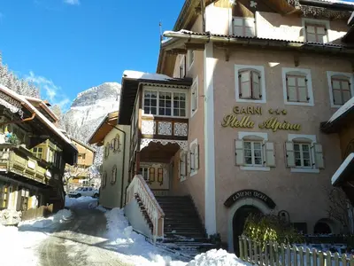 a building with stairs in the snow next to a mountain at Garnì Stella Alpina in Canazei