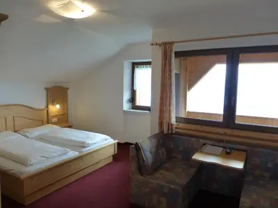 a bedroom with a bed and a chair and a window at Berggasthof Häusler in San Lorenzo di Sebato
