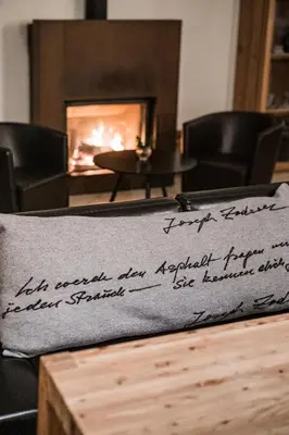 a pillow with writing on it in front of a fireplace at Hotel Hurtmuehle Kronblick in San Lorenzo di Sebato