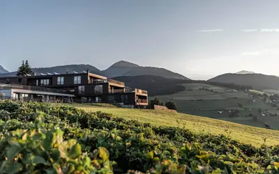 a house on a hill with mountains in the background at Aparthotel Panorama Living Dolomites in Maranza