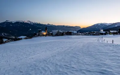 a snow covered mountain with a church in the distance at Aparthotel Panorama Living Dolomites in Maranza