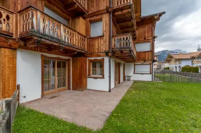 a wooden house with a balcony and a yard at Casa De La Veisc in Pozza di Fassa