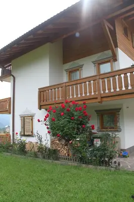 a house with a balcony with red flowers on it at Garnì Goccia d'Oro in Cavalese