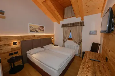 a bedroom with a white bed and a wooden ceiling at Hotel Tita Piaz in Canazei