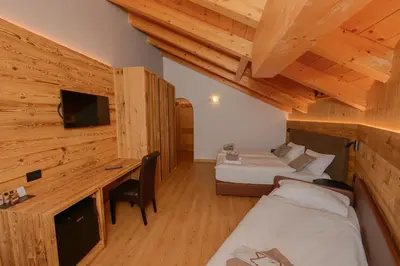 a room with two beds and a desk and a television at Hotel Tita Piaz in Canazei