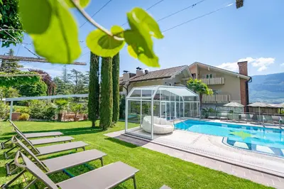 a mansion with a swimming pool and a glass house at Tirolerin Garni Hotel in Termeno