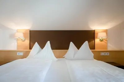 a large white bed with white pillows on it at Tirolerin Garni Hotel in Termeno