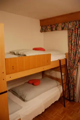 a bedroom with two beds and a table with red pillows at Albergo Genziana in San Vigilio Di Marebbe