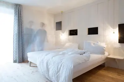 a white bedroom with a bed and a person in the background at Frida am Wald in Rasùn di Sotto