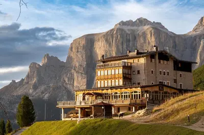 a building on a hill with a mountain in the background at Hotel Pordoi Passo Pordoi Vegetarian Hotel in Canazei