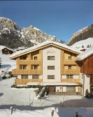 a large building in the snow with mountains in the background at Residence Settsass in Colfosco