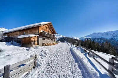 a snow covered road in front of a wooden building at Hotel Dolomiten in Monguelfo