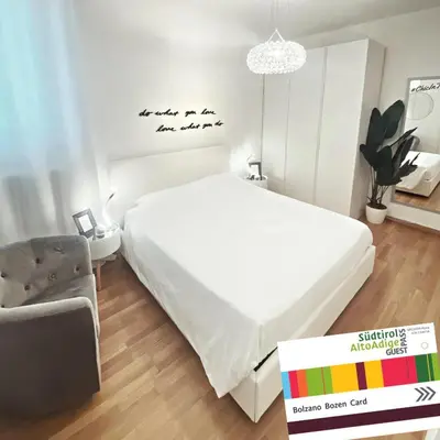 a white bedroom with a white bed and a chair at Chic In The City in Bolzano