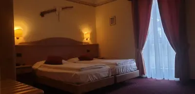 two beds in a hotel room with a window at Albergo Bernard in Canazei