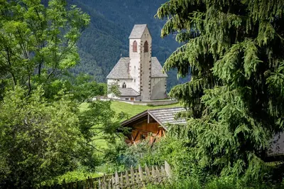 a church on a hill with a fence and trees at Oberpiskoihof in Funes