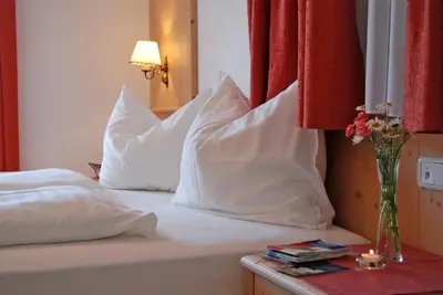 a bed with white pillows and a vase of flowers on a table at Gasthof Weidmannshof in Bressanone