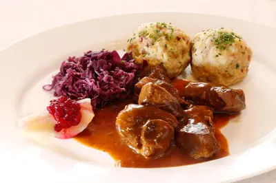 a white plate of food with meat and vegetables at Hotel Hubertusstube in Laion