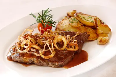a white plate of food with steak and potatoes at Hotel Hubertusstube in Laion