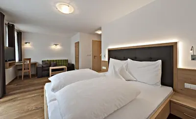 a bedroom with a large white bed and a living room at Hotel Pfandleralm in San Martino