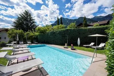 a swimming pool with lounge chairs and an umbrella at Garni Hotel Kessler in Tirolo