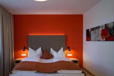 a bedroom with a bed with an orange wall at Garni Hotel Kessler in Tirolo