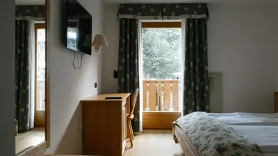 a bedroom with a bed and a desk and a window at Hotel Malga Passerella in Moena