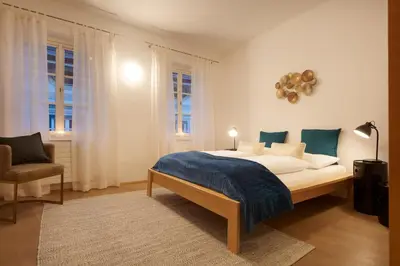 a bedroom with a bed and a chair and windows at Franciscus Apartments in Bolzano