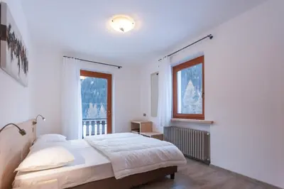a white bedroom with a bed and a window at Casa Zulian in Falcade