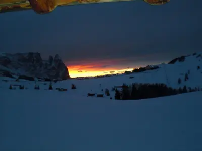 a sunset in the snow with the sun setting in the background at Appartements Karbon in Seiser Alm