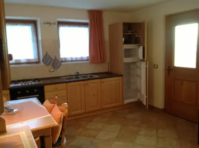 a kitchen with a sink and a table and windows at Appartamenti Piazzi in Tesero