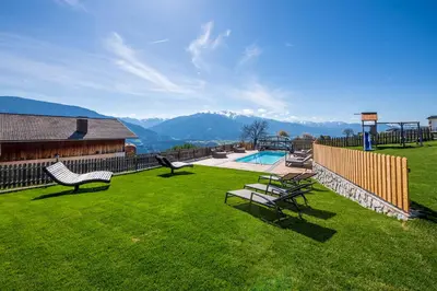 a yard with chairs and a pool with mountains in the background at Der Brunnerhof in Mühlbach
