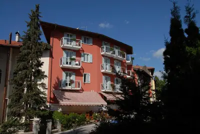 a red building with white balconies on a street at Hotel Sport in Coredo