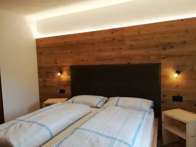 two beds in a bedroom with a wooden wall at Aria d'Bosch in Badia