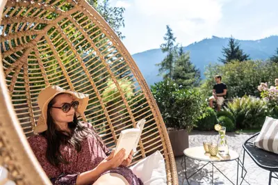 a woman sitting in a wicker chair reading a book at Hotel Paradies in Tires